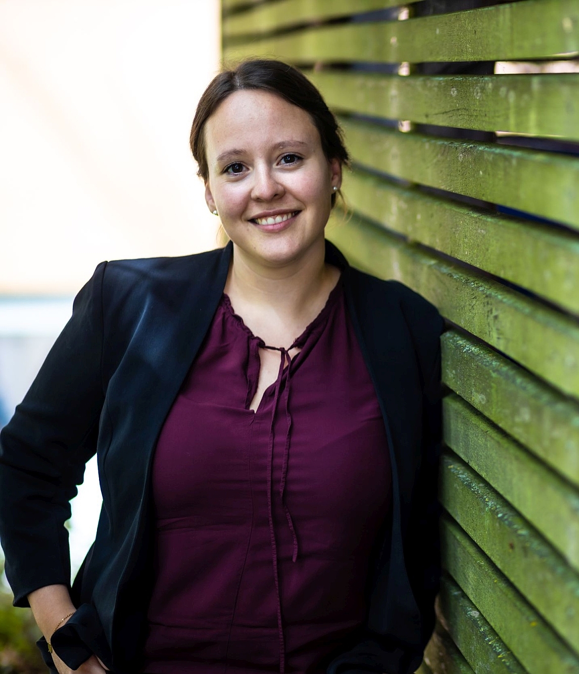 Junge Frau lehnt an einer Wand aus grünen Holzleisten