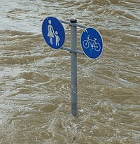 Überfluteter Weg Metallstange mit je einem Schild "Fußgänger" und "Radfahrer", noch circa einen Meter über dem Hochwasserspiegel, rundum braunes Wasser