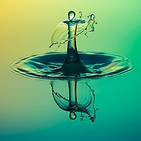 Wassertropfenfigur in menschlicher Gestalt? Glattes Wasser, links oben gelb, Mitte und rechts unten türkisgrün mit Wassertropfen, der gerade eingetaucht ist und an der Eintauchstelle beim Austreten eine menschlich anmutende Figur mit Schleier bildet