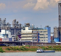 Industriewerk mit Raffinerie, im Vordergrund ein Fluss mit Lastenkahn