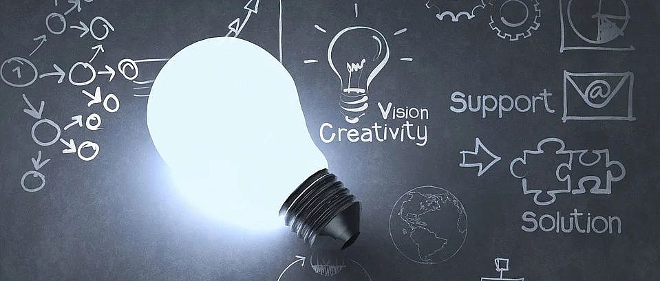 Weiße Glühbirne vor schwarzem Hintergrund mit Zeichnungen und englischen Worten