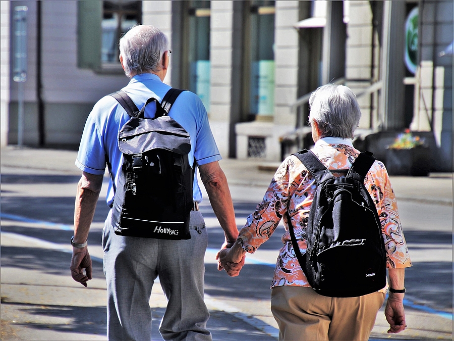 Älterer Herr und ältere Dame die Händchenhaltend durch die Stadt laufen