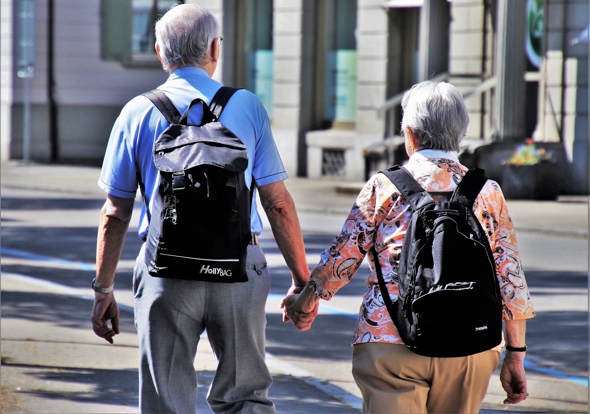 Älterer Herr und ältere Dame die Händchenhaltend durch die Stadt laufen 