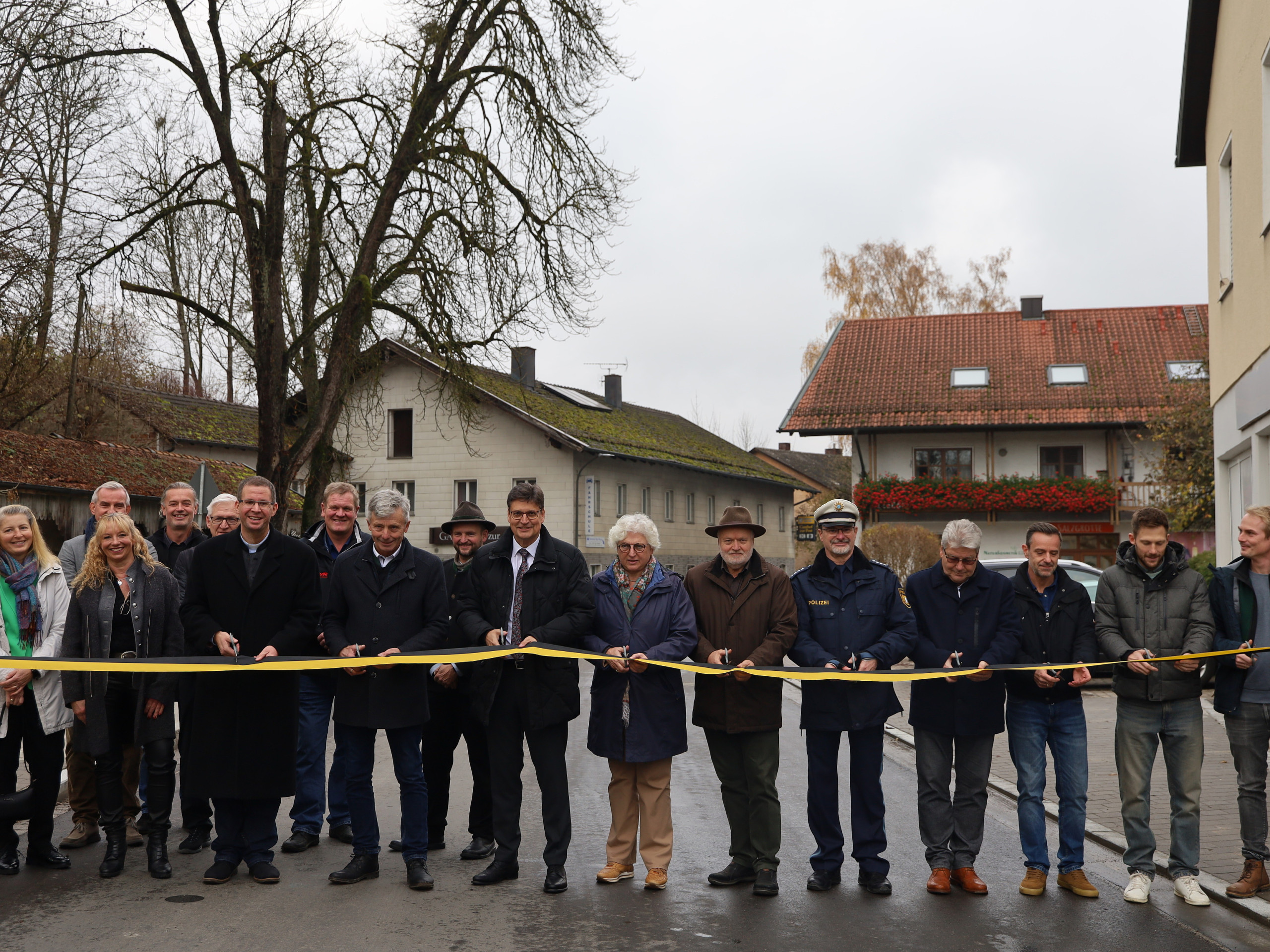 : Ein gemeinsamer Schnitt zur offiziellen Freigabe der Brücke: (Personen mit Schere von links) Pfarrer Michel Seifert, Andreas Maierhofer (2. Bürgermeister Gemeinde Polling), Landrat Max Heimerl, stv. Landrätin Ilse Preisinger-Sontag, Bürgermeistersprecher Thomas Einwang, Karl-Heinz Stocker von der Polizei Mühldorf, Peter Weber (IGL, PUTZ + PARTNER mbB Beratende Ingenieure), Robert Martinez (Tiefbauleiter Landratsamt Mühldorf a. Inn), Martin Gebler (Ingenieurbüro Behringer & Partner mbB), Martin Höpp (Fa. Hagn Umwelttechnik GmbH)