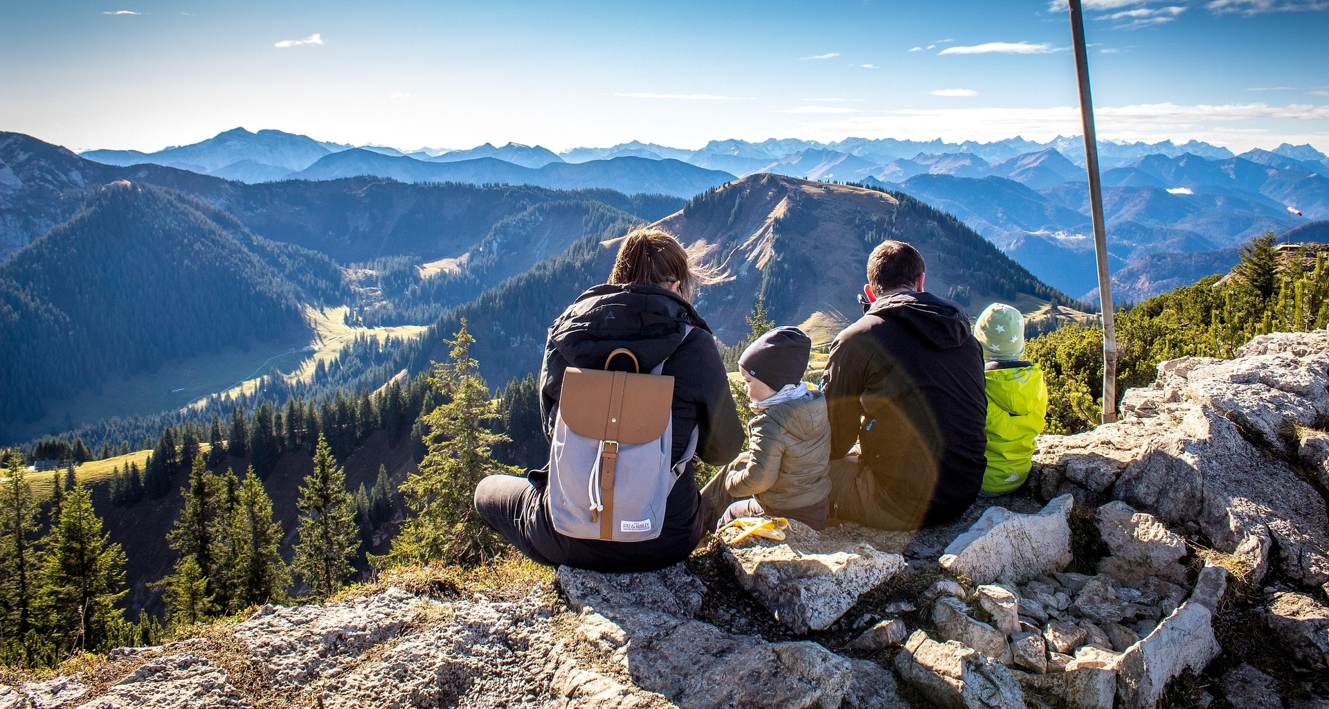 Familie sitzt auf einem Berggipfel und blickt in die Ferne