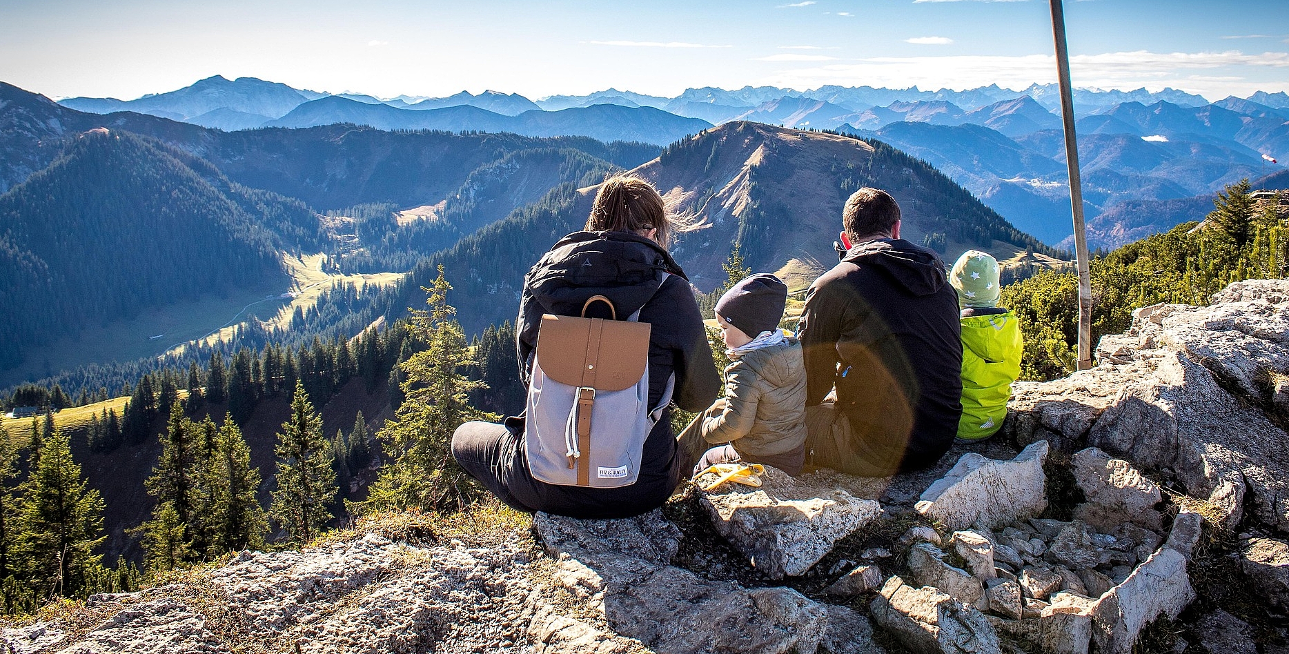 Familie sitzt auf einem Berggipfel und blickt in die Ferne