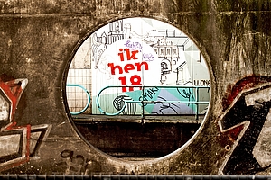 Blick durch ein Loch einer Mauer auf ein Graffiti