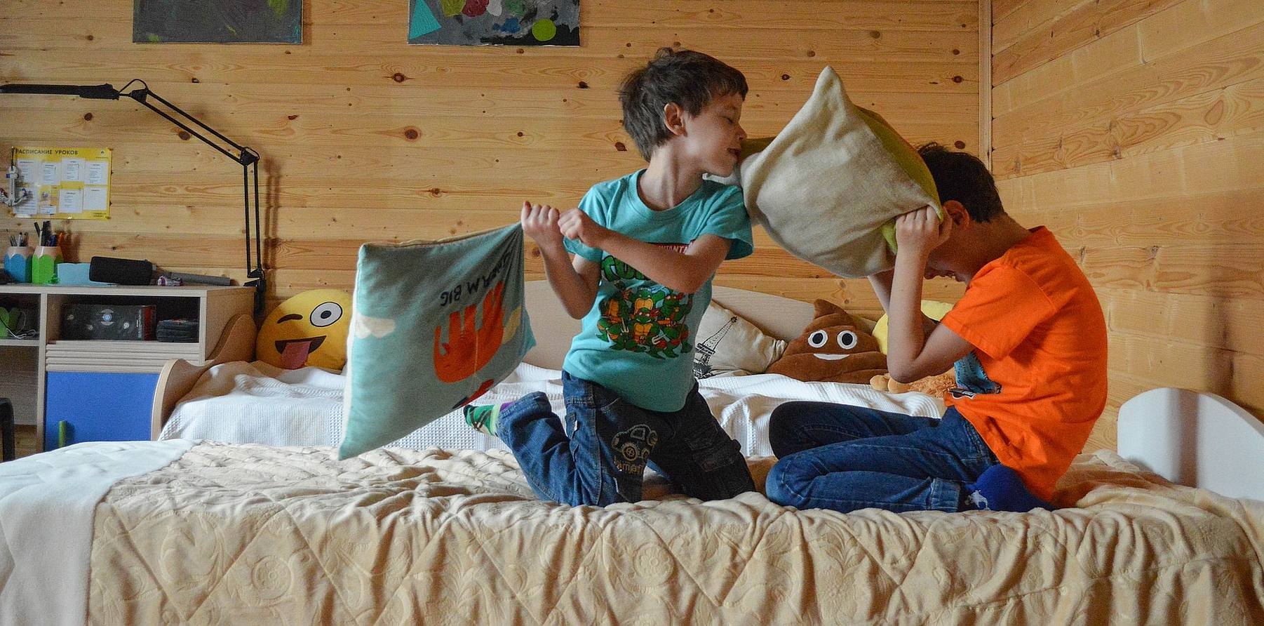 zwei Jungen sitzen auf einem Bett und machen eine Kissenschlacht