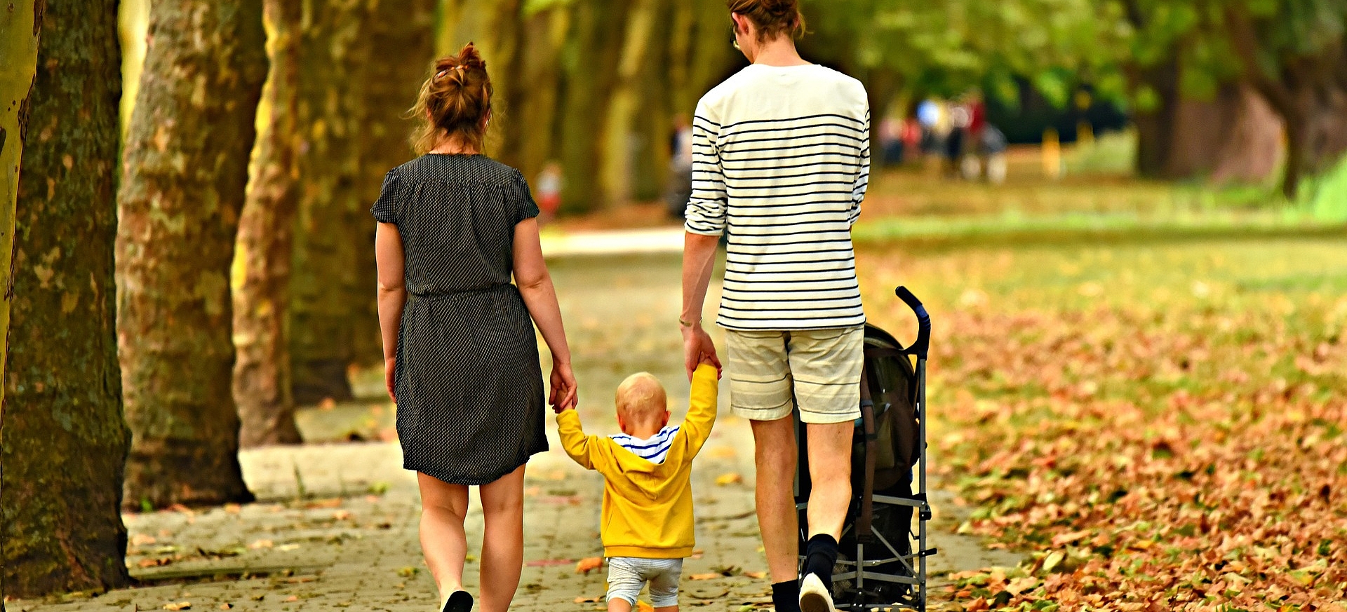 Mutter und Vater gehen mit Kleinkind und Kinderwagen spazieren.