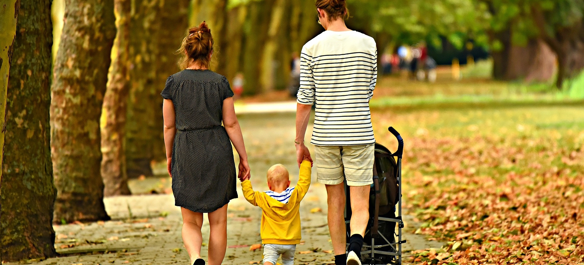 Mutter und Vater gehen mit Kleinkind und Kinderwagen spazieren.