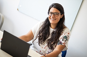 Frau mit Brille und dunklen langen Haaren sitzt vor einem Laptop