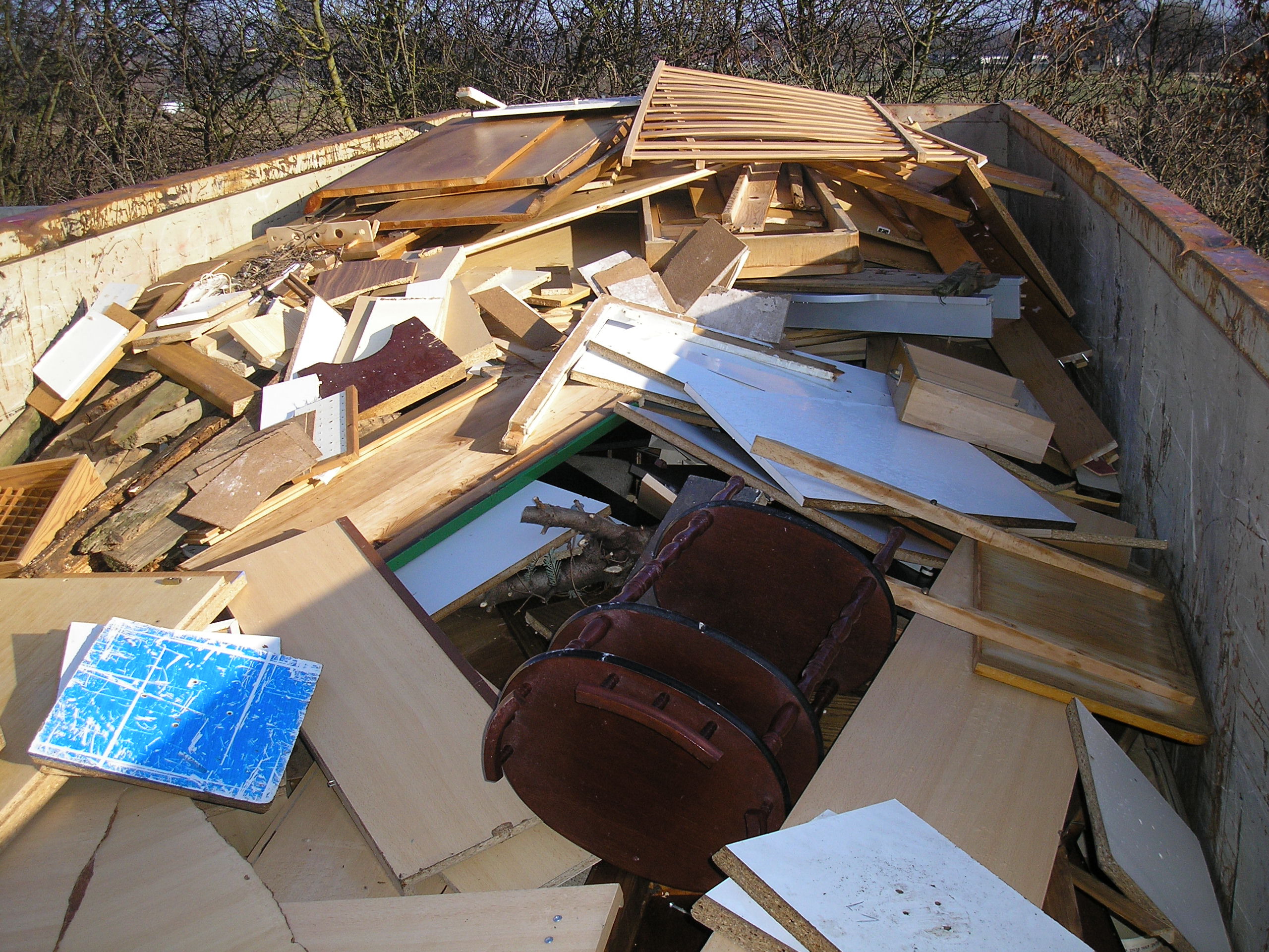 Container, der befüllt ist mit verschiedenen Gegenständen aus Holz, wie z. B. Lattenroste, Holzmöbel, Holzplatten, Holzregale.