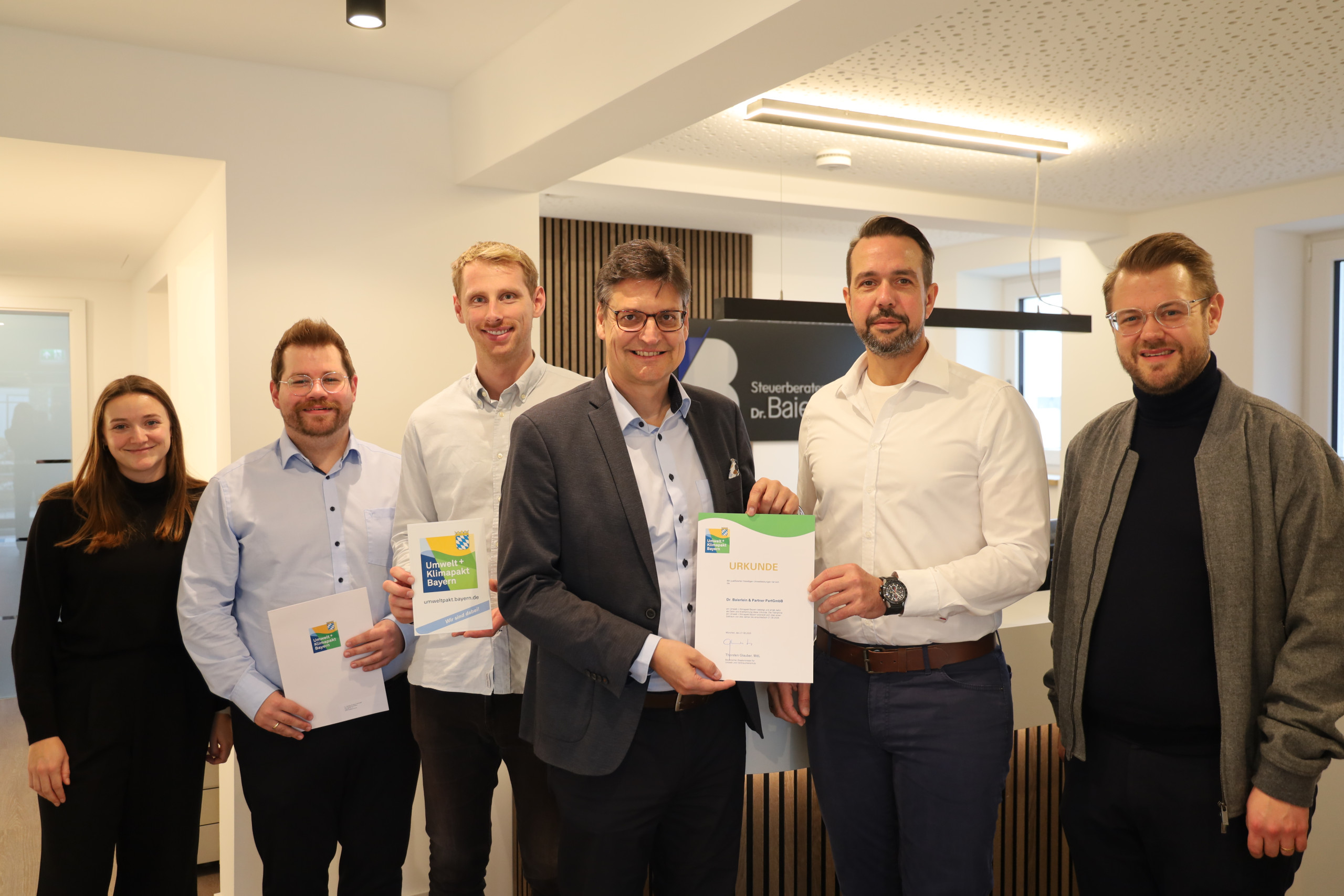 (von links nach rechts): Michaela Linner (Wirtschaftsförderung Landkreis Mühldorf a. Inn), Wirtschaftsförderer Thomas Perzl, Johannes Maier (Partner Dr. Baierlein & Partner), Landrat Max Heimerl, Stephan Kretzschmar (Partner Dr. Baierlein & Partner) und Bürgermeister Michael Hetzl bei der Übergabe der Urkunde zum Umwelt- und Klimapakt Bayern.