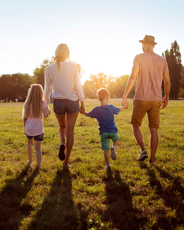 Familie von hinten geht in Richtung Sonnenuntergang