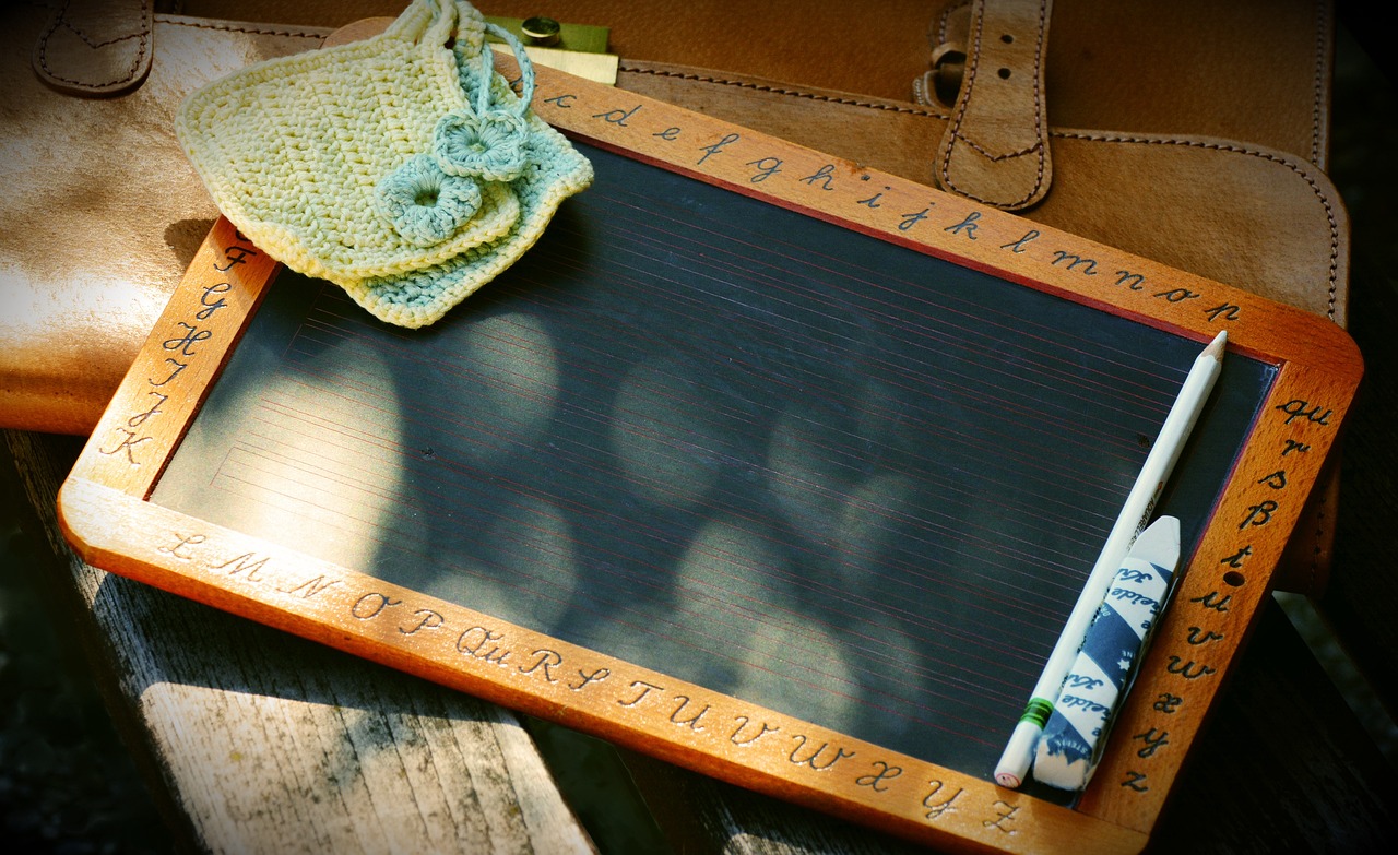 Kleine Tafel mit Buchstaben im Rahmen, auf einer Ledertasche liegend.