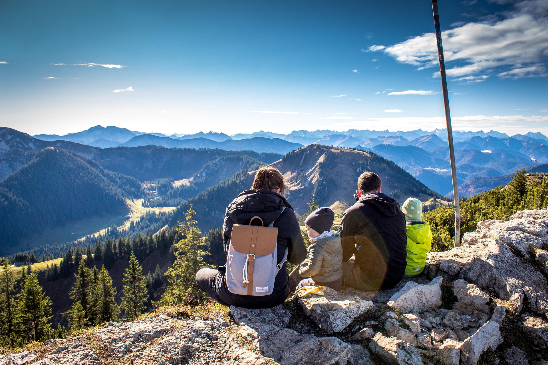 Familie sitzt auf einem Berggipfel und blickt in die Ferne
