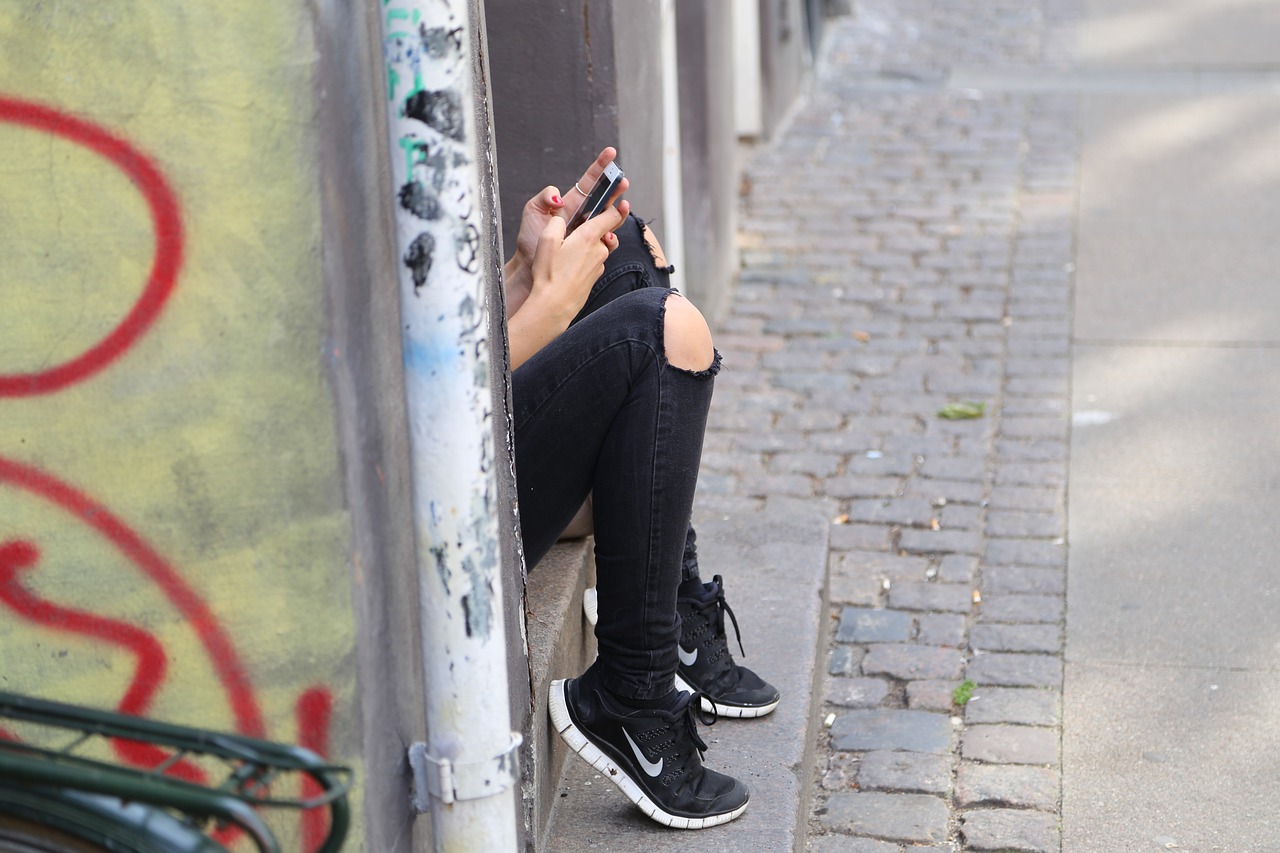 Jugendliche sitzt in einem Hauseingang und hat ein Smartphone in der Hand