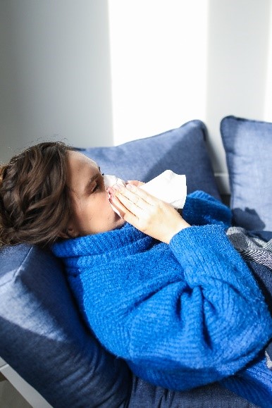 Frau mit blauem Pullover und Schnupfen auf dem Sofa liegend