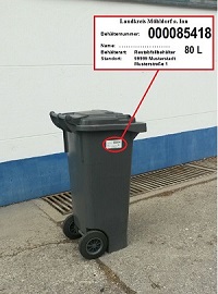 schwarze Mülltonne mit weißem Etikett mit Behälternummer und Adresse